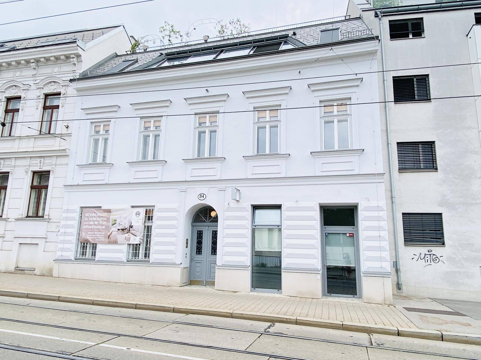 Klassische weiße Fassade eines Mehrfamilienhauses mit großen Fenstern und Jalousien.