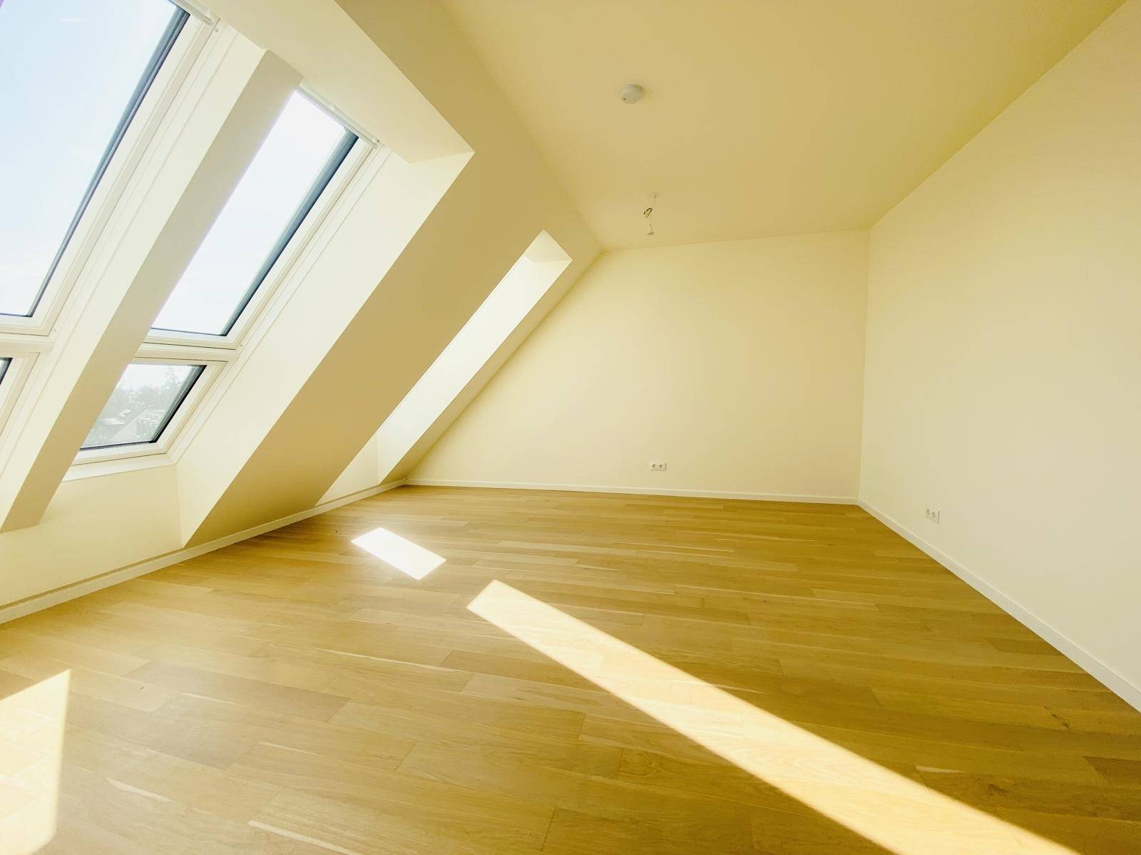 Geräumiges Dachgeschosszimmer mit schrägen Wänden, Holzparkettboden und viel natürlichem Licht.