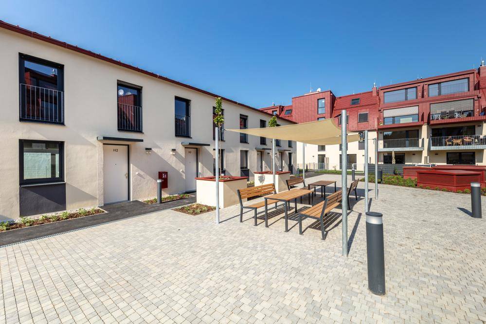 Gemeinschaftlicher Innenhof mit Sitzgelegenheiten und Sonnenschutz, umgeben von Wohngebäuden.