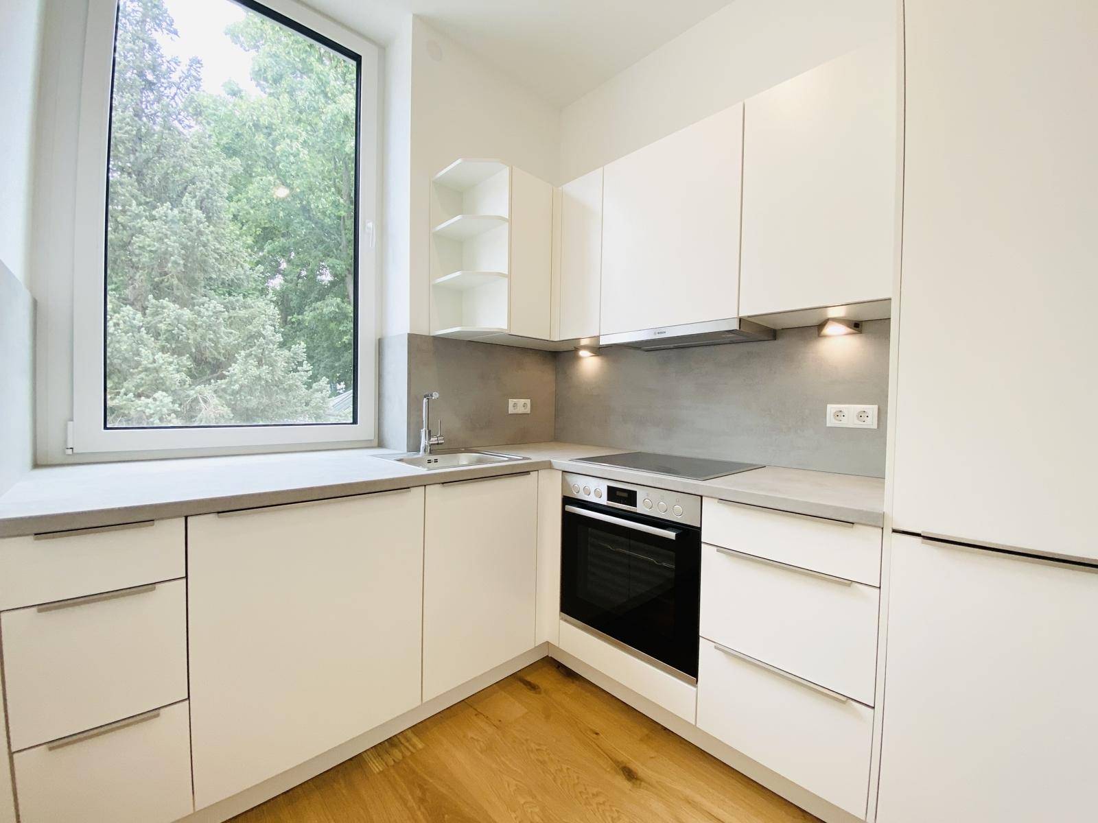 Moderne Einbauküche mit weißen Schränken, Induktionskochfeld und Fenster mit Grünblick.