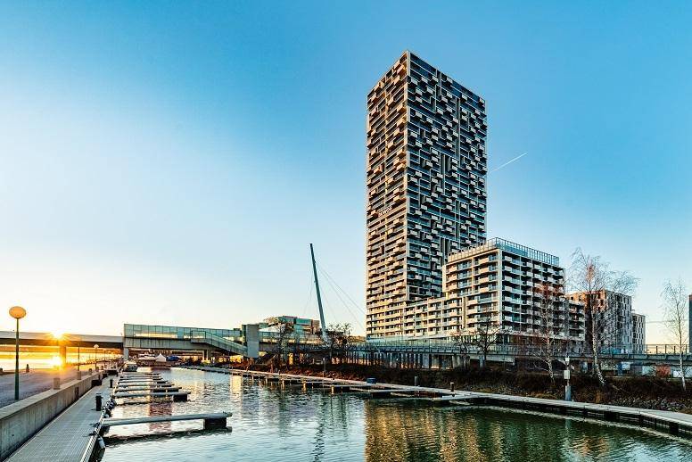 Modernes Hochhaus am Wasser mit markanter Architektur und vielen Balkonen.