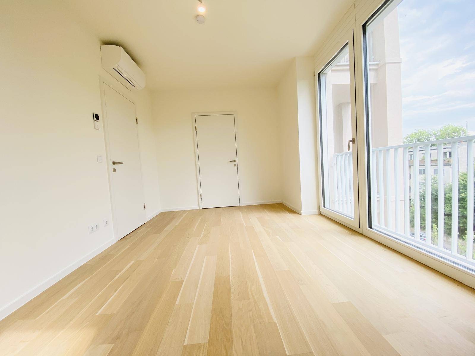 Geräumiges, helles Zimmer mit Parkettboden, Klimaanlage und Zugang zu einem Balkon.