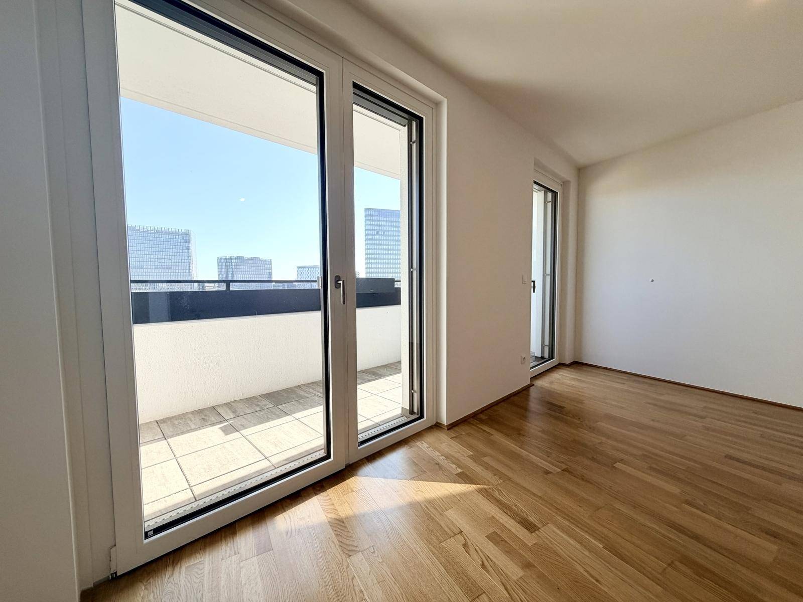 Lichtdurchfluteter Raum mit Holzboden und Balkonzugang, ideal für Wohnzwecke.