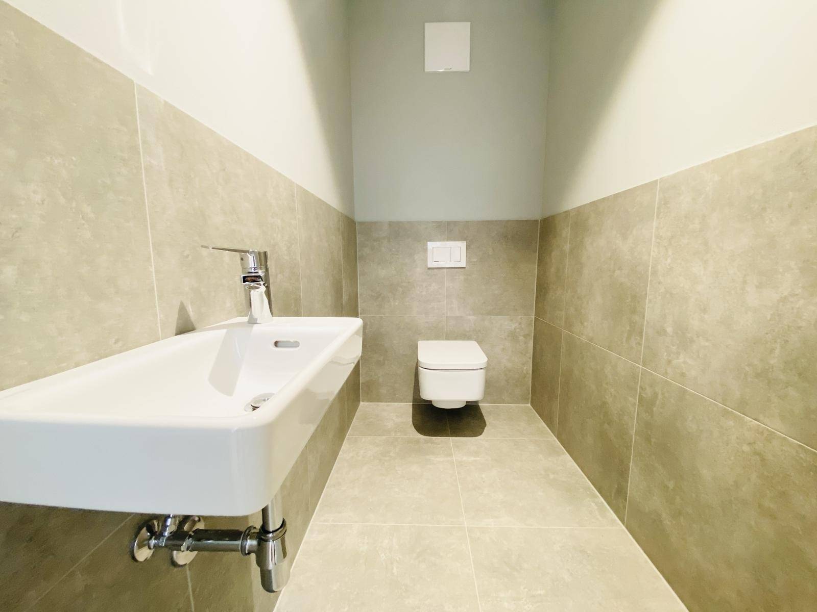 Modernes Gäste-WC mit Wand-WC und kleinem Waschbecken, in neutralen Farben gehalten.