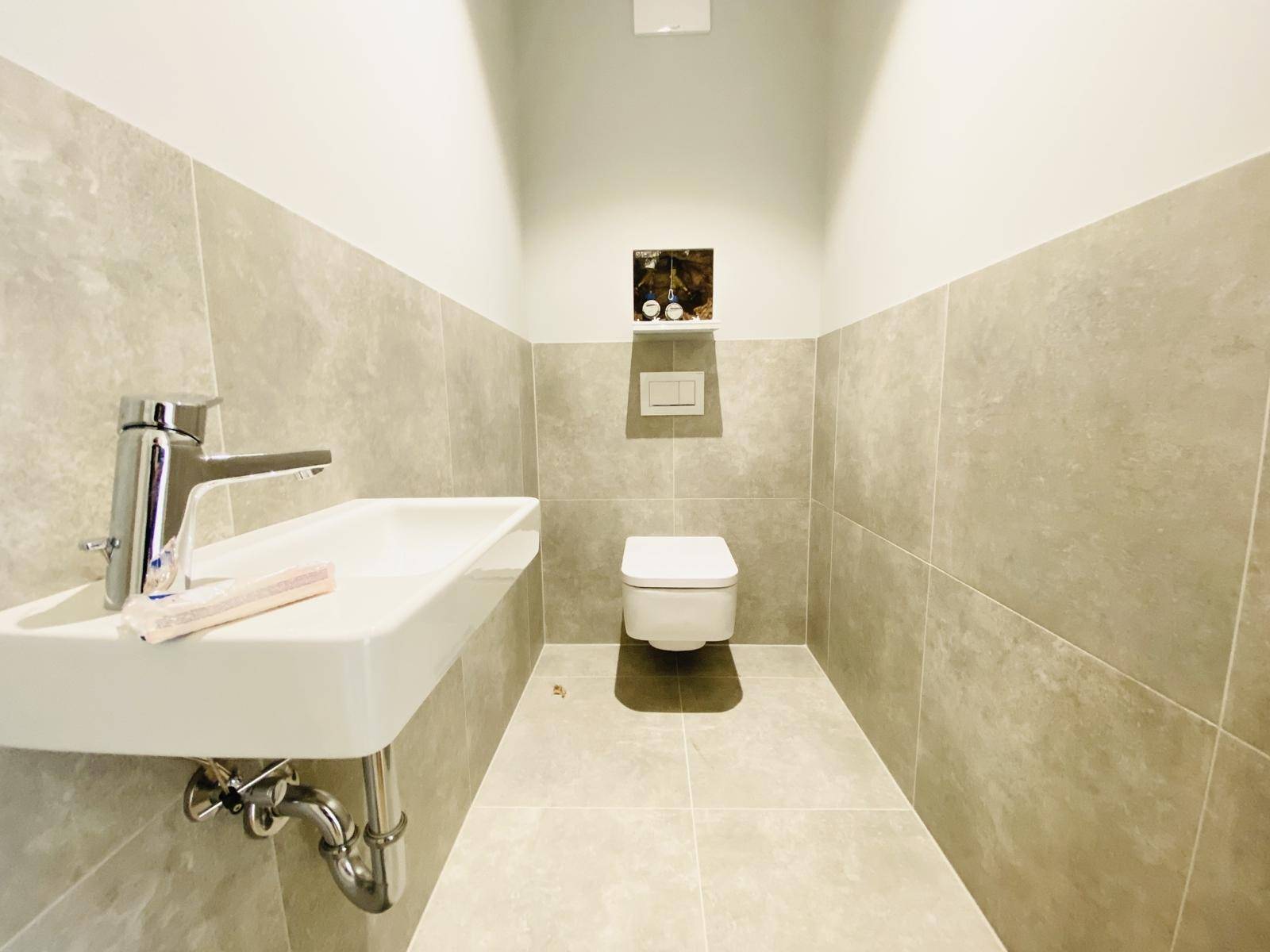 Modernes Gäste-WC mit Wand-WC, Waschbecken und grauen Fliesen.