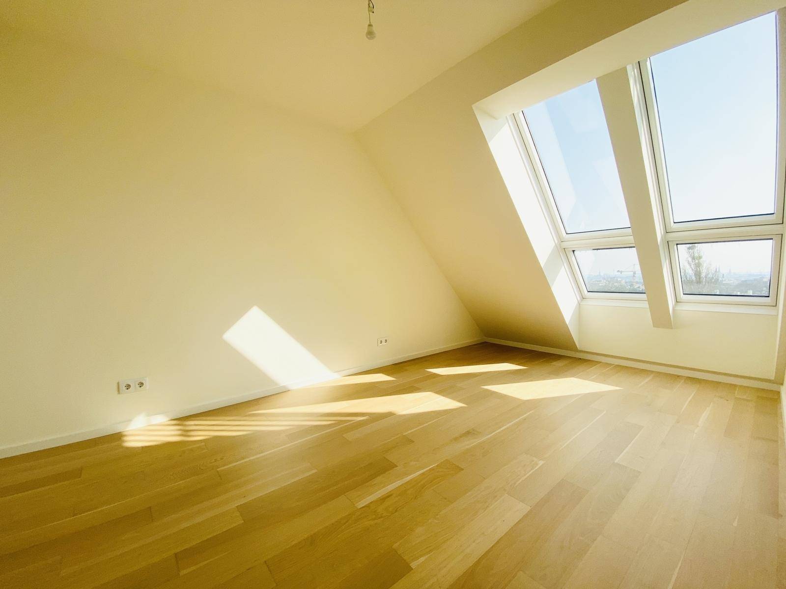 Helles Zimmer im Dachgeschoss mit Holzboden, Dachschräge und großen Schrägfenstern.