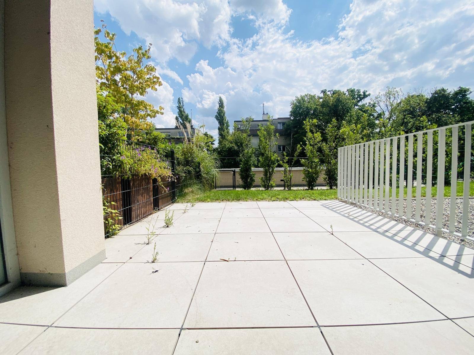 Helle, geflieste Terrasse mit seitlichem Zugang zum Garten und einer modernen weißen Balustrade.