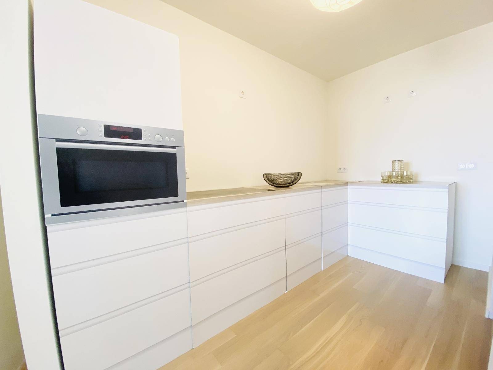 Moderne Einbauküche mit weißen Fronten, integriertem Backofen und Holzboden.