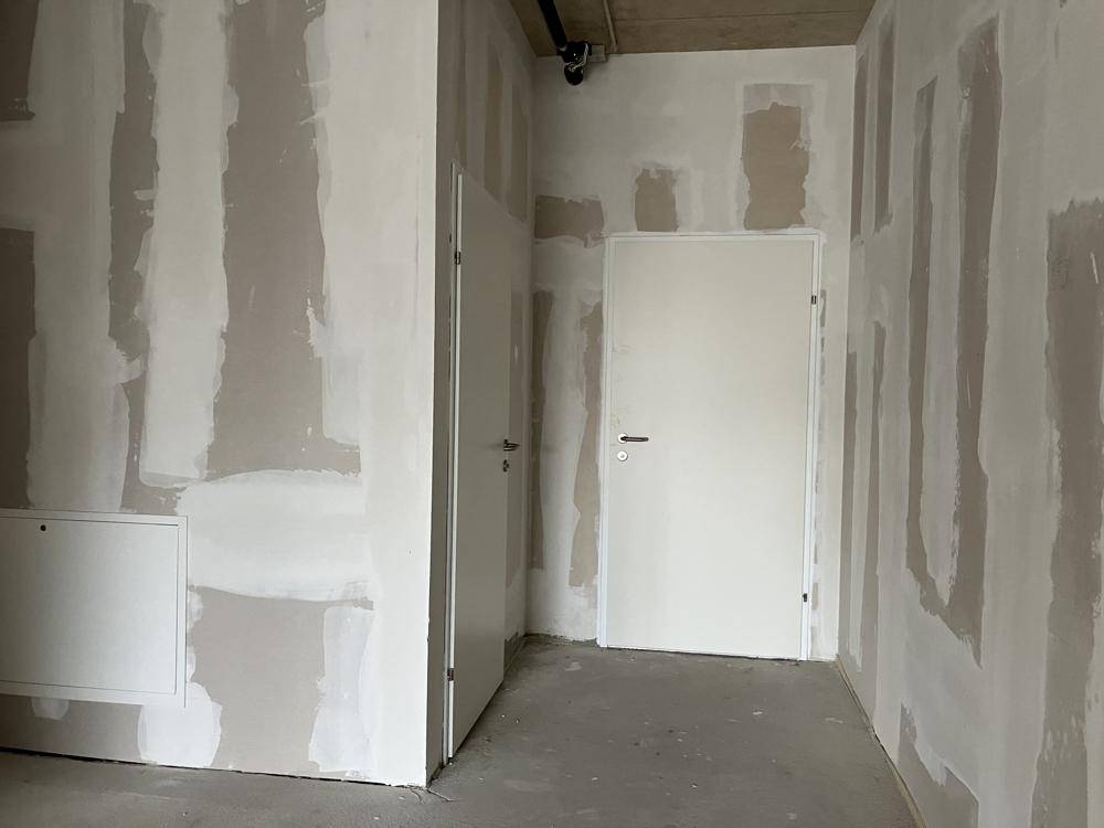 Innenraum im Rohbau mit zwei Türen und unfertigen Wänden, bereit für den finalen Ausbau.