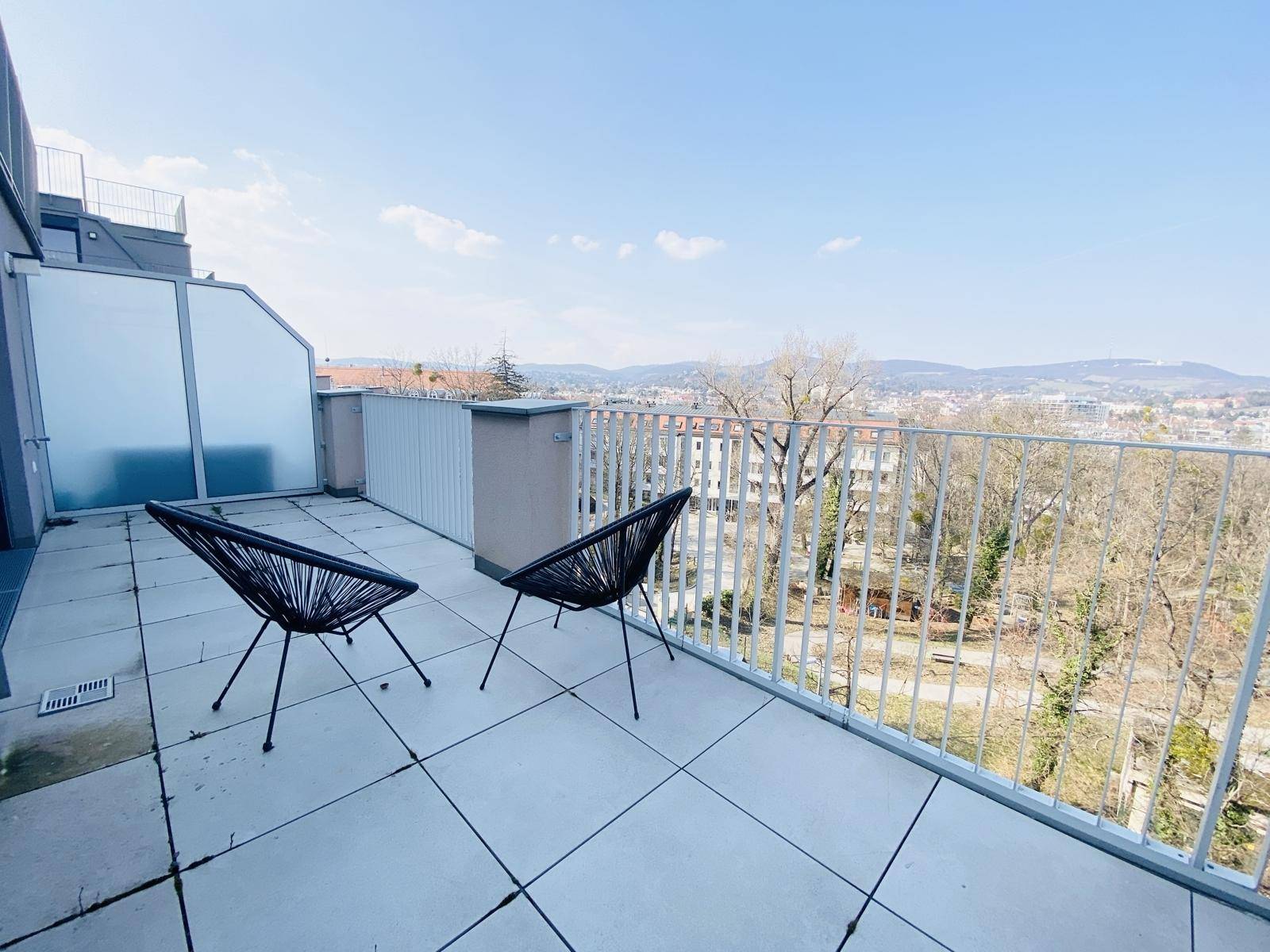Sonniger Balkon mit Fliesenboden und Blick auf die grüne Umgebung und die Stadt.