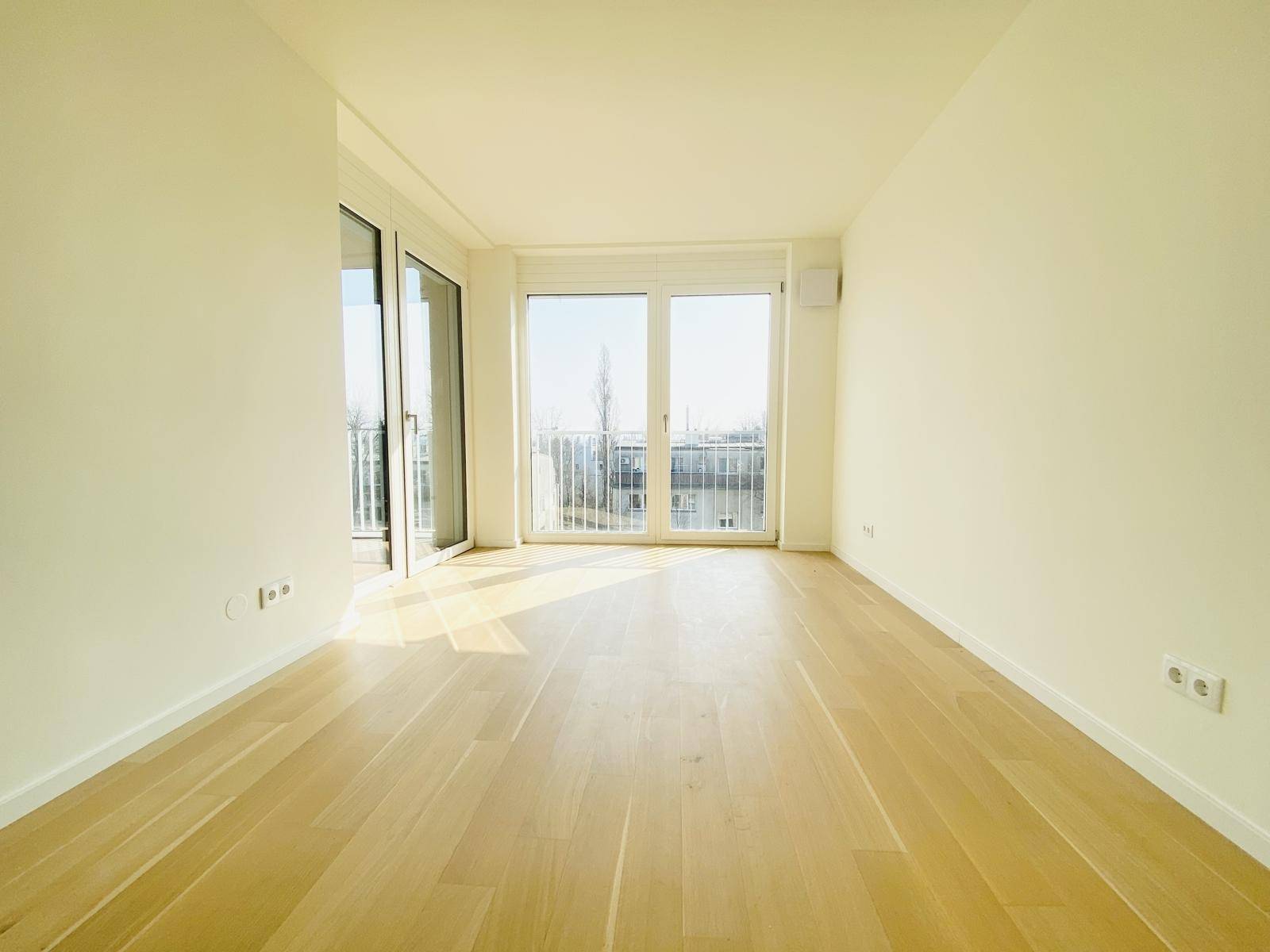 Helles Zimmer mit Holzboden und großen Fenstern, die viel Tageslicht hereinlassen.