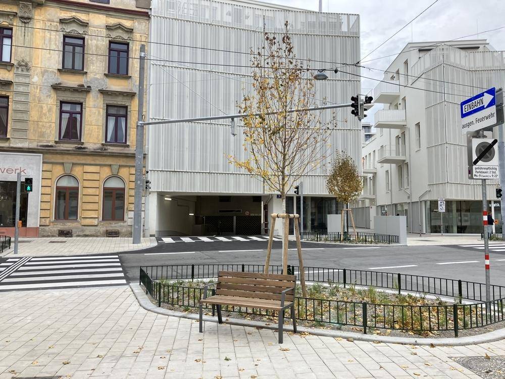 Moderne Gebäudefassade mit Tiefgarageneinfahrt und umliegender Stadtansicht.