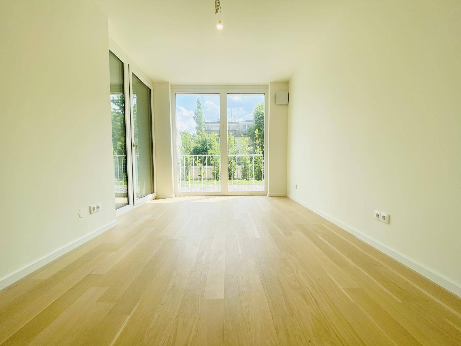 Helles Zimmer mit Parkettboden und großen Fenstern, die viel Tageslicht hereinlassen.