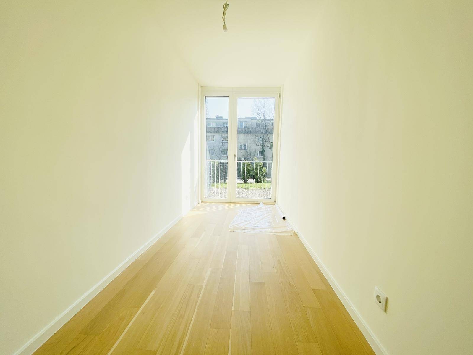 Lichtdurchflutetes Zimmer mit Parkettboden und großem Fenster, das viel Tageslicht hereinlässt.