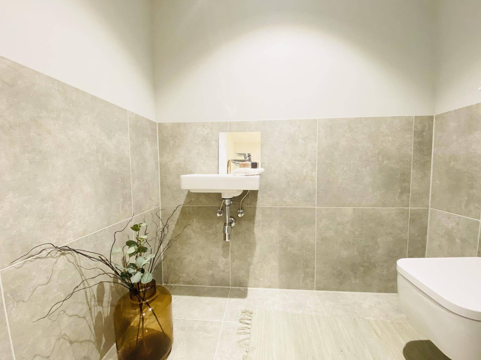 Modernes Gäste-WC mit Wand-WC, kleinem Waschbecken und grauen Fliesen an Wänden und Boden.