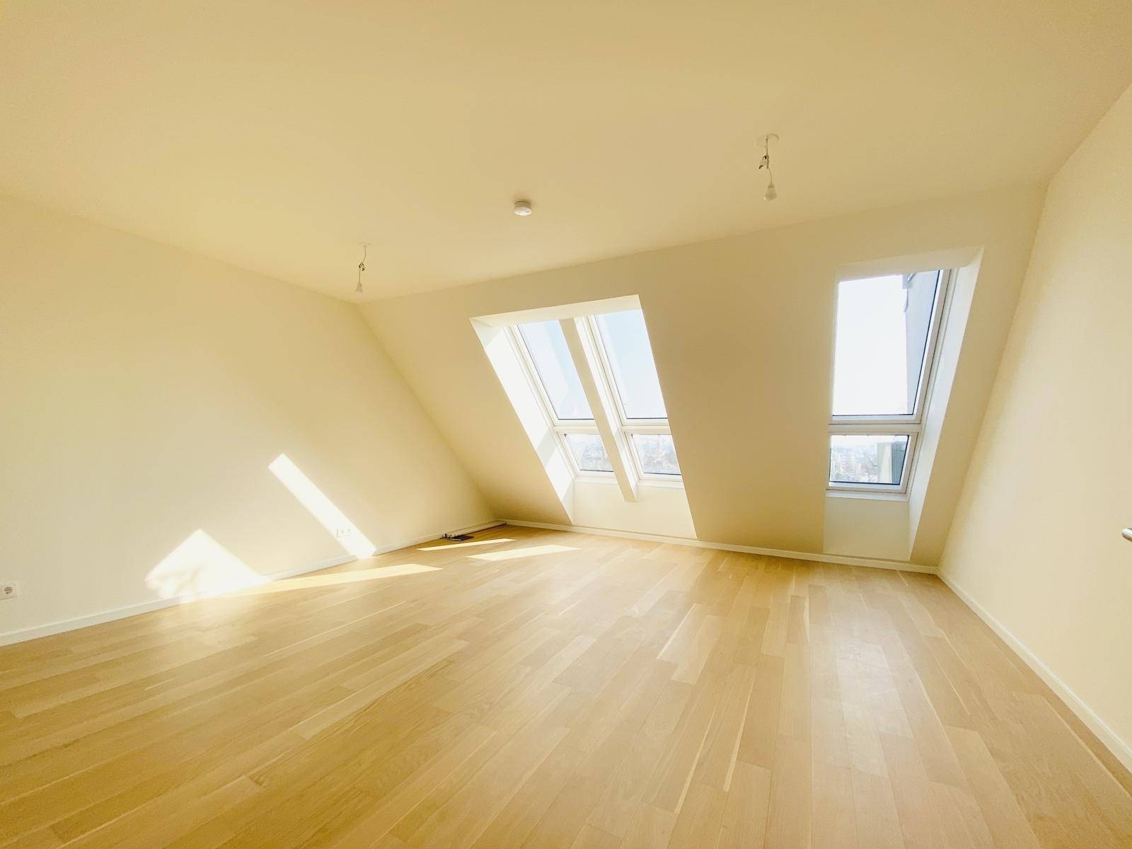 Geräumiges Dachgeschosszimmer mit schrägen Wänden, Holzparkettboden und viel natürlichem Licht.