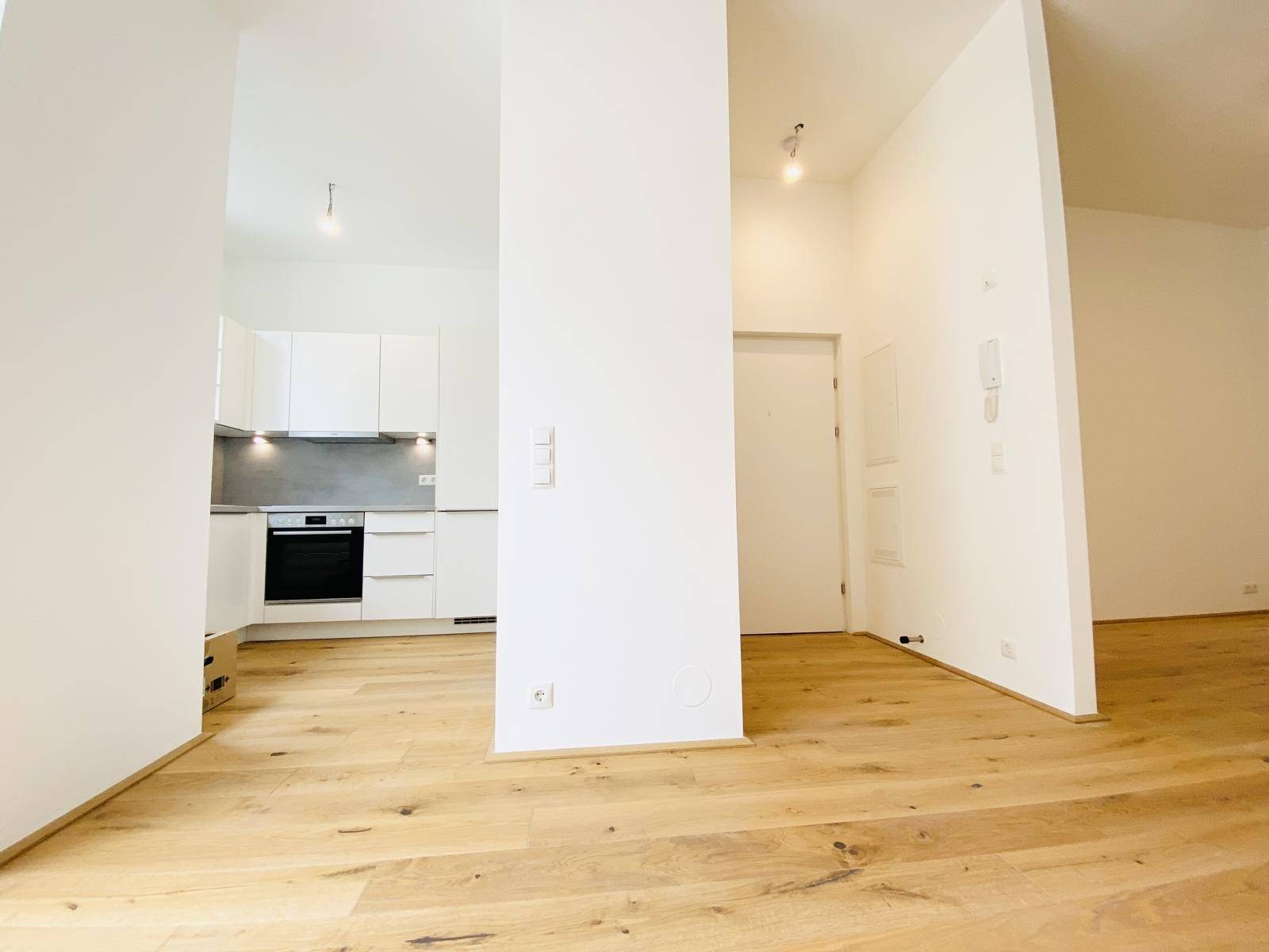 Offener Wohnbereich mit Holzboden, weiß gestrichenen Wänden und Blick zur Küche.