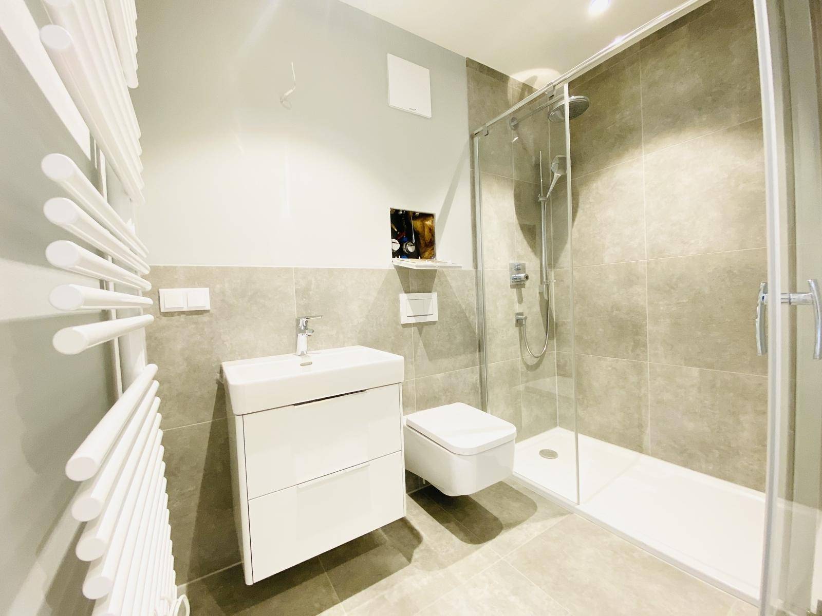 Modernes Badezimmer mit Dusche, Wand-WC und beheiztem Handtuchhalter in neutralen Farben.