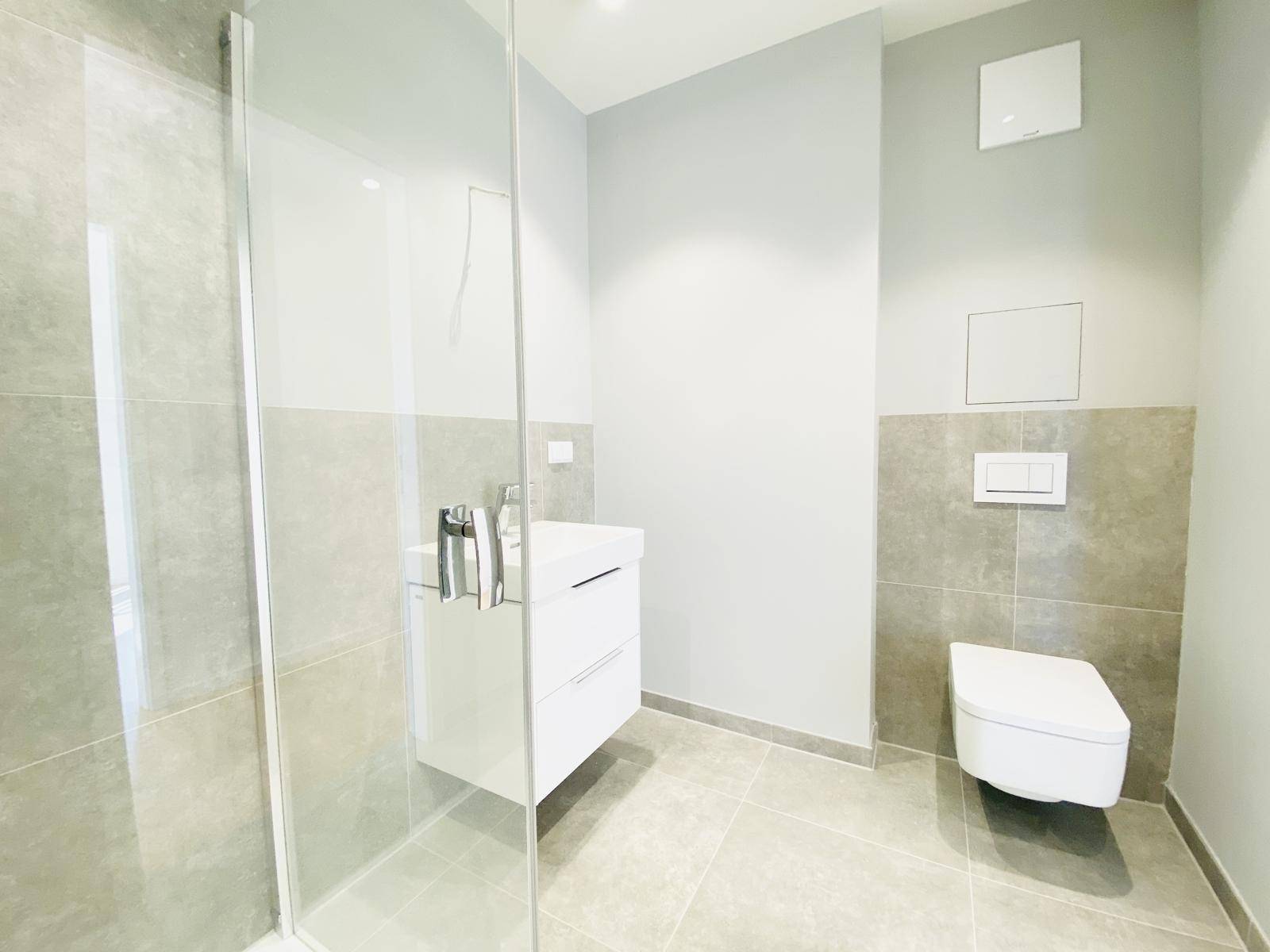 Elegantes Badezimmer mit wandhängendem WC, modernem Waschtisch und grauen Fliesen.