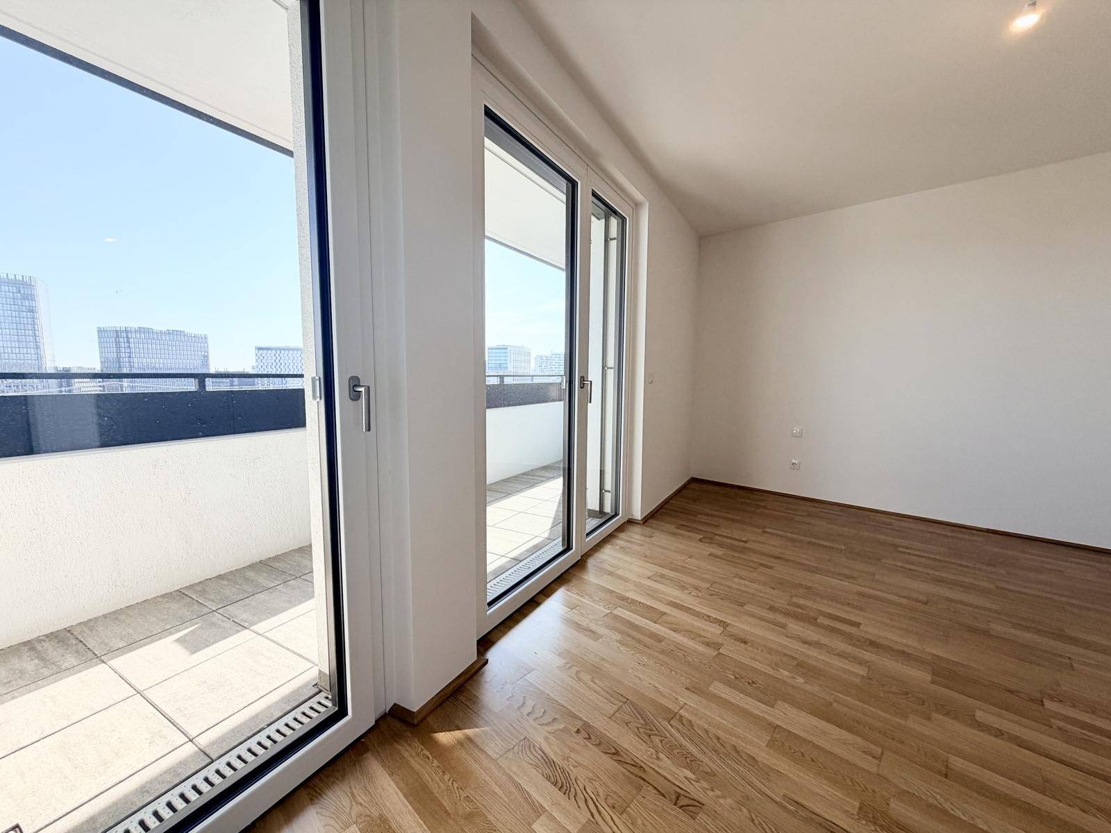 Helles Zimmer mit Holzboden und Zugang zu einem Balkon mit Stadtblick.