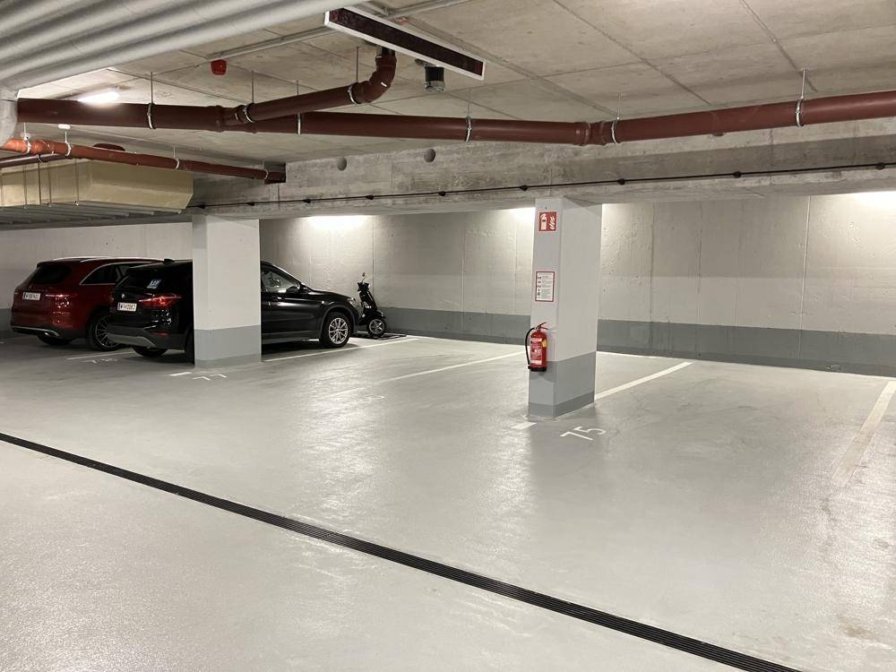 Tiefgarage mit breiten Fahrspuren, nummerierten Parkplätzen und Brandschutzvorrichtungen.
