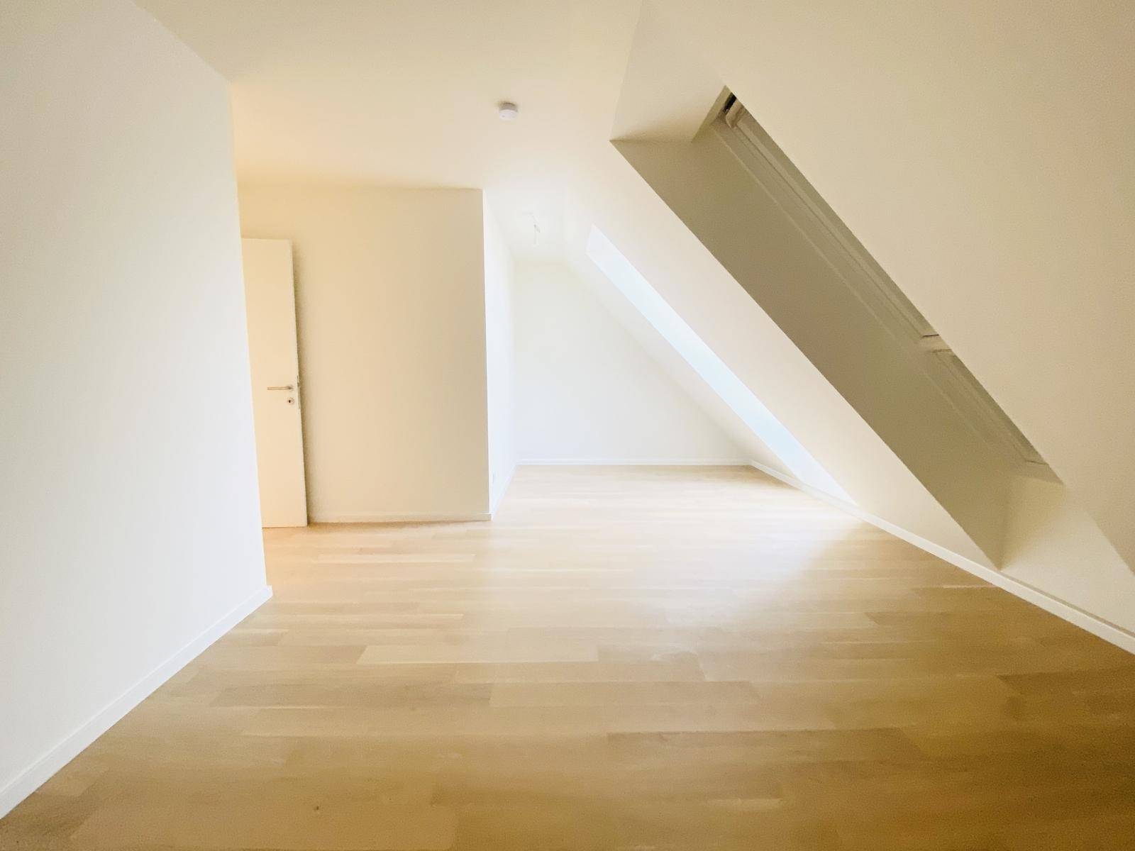 Heller Flur im Dachgeschoss mit Holzparkettboden und schrägen Wänden, der zu weiteren Räumen führt.
