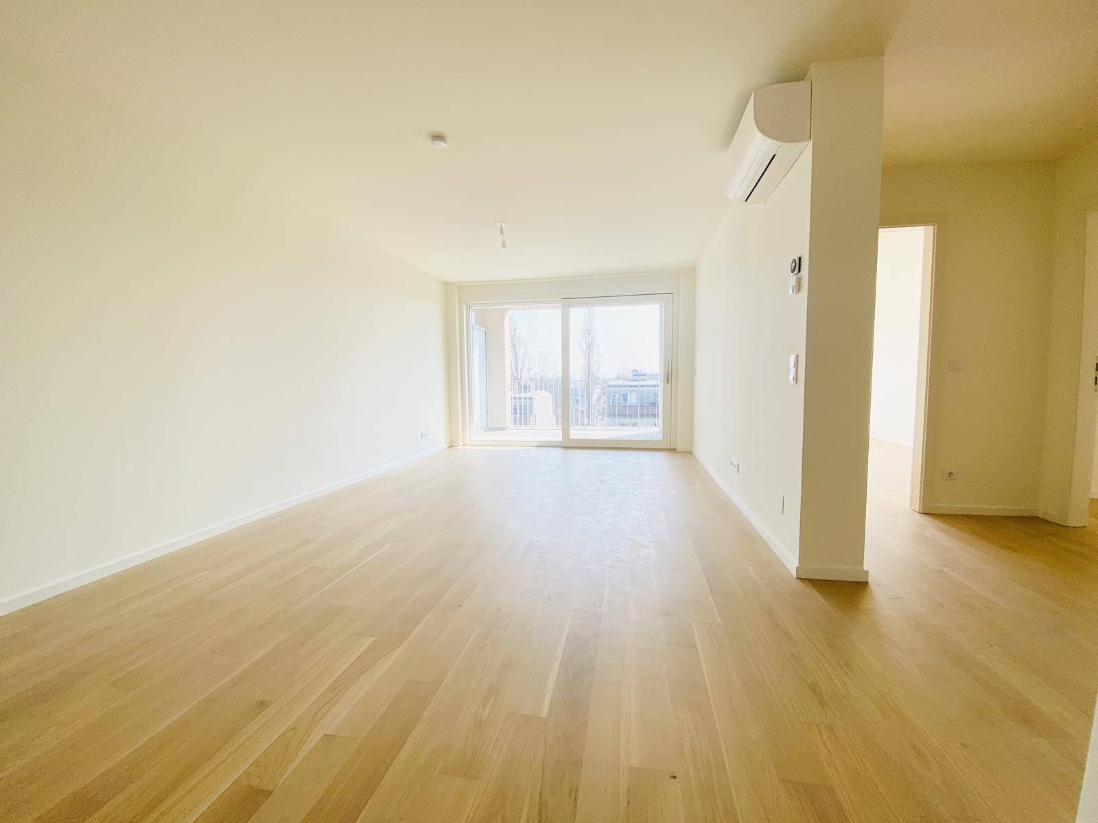 Heller Wohnraum mit Holzboden, Klimaanlage und Zugang zu einem sonnigen Balkon.