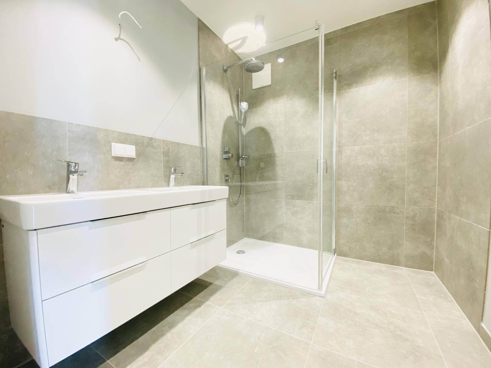 Modernes Badezimmer mit begehbarer Dusche, Doppelwaschbecken und grauen Fliesen.