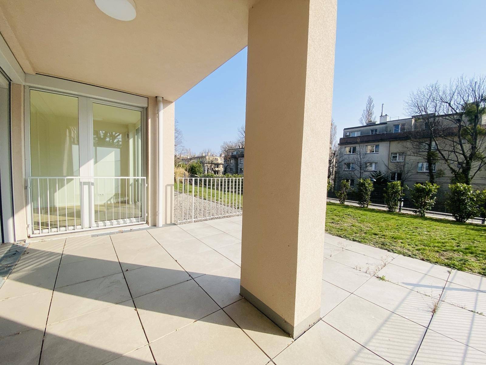 Sonniger Terrassenbereich mit großen Schiebetüren zum Innenraum und Blick ins Grüne.