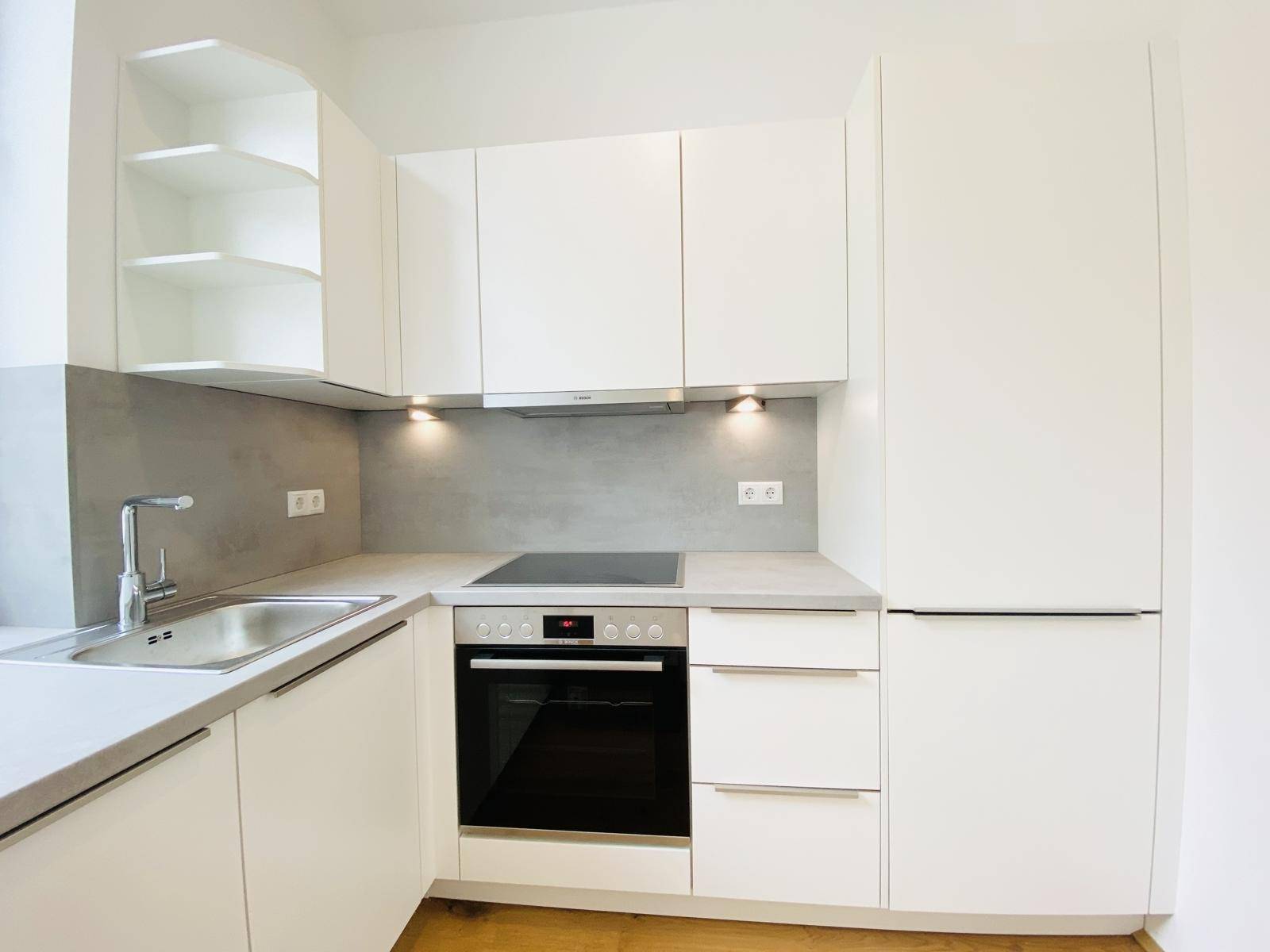 Kompakte, moderne Einbauküche mit weißen Fronten, integrierten Geräten und Holzboden.