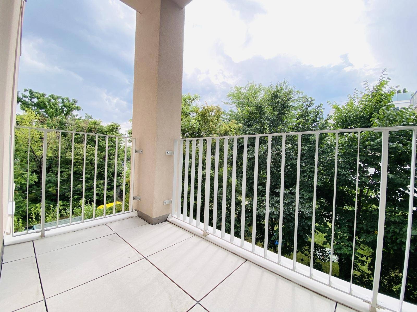Geräumiger Balkon mit Fliesenboden und Blick auf grüne Bäume und die Umgebung.