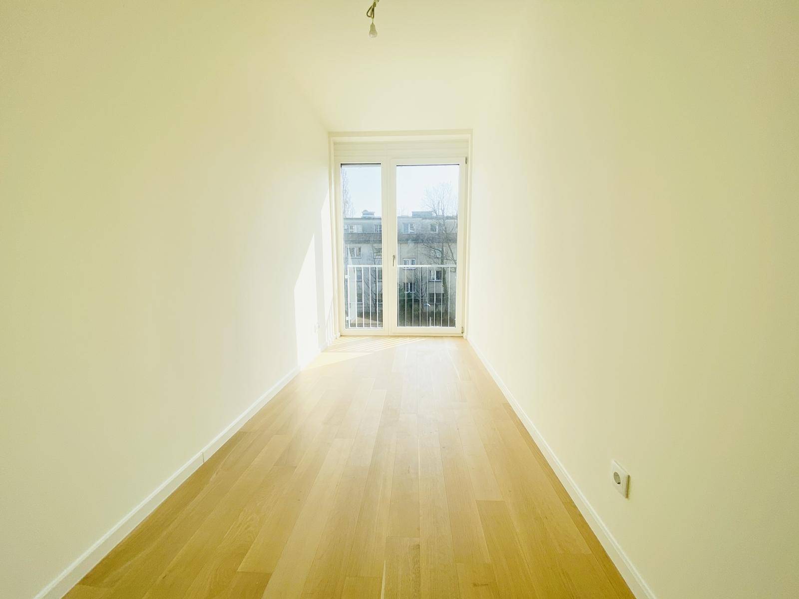 Helles, leeres Zimmer mit Parkettboden und Zugang zu einem französischen Balkon.