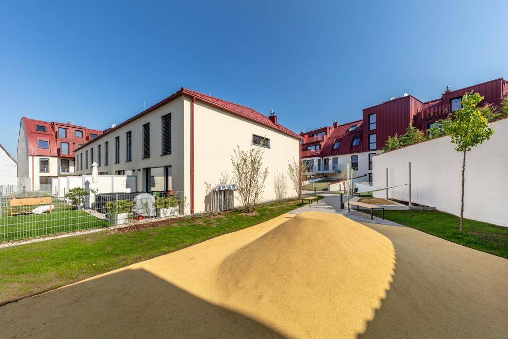 Außenbereich der Wohnanlage mit Spielplatz und Grünflächen, umgeben von modernen Gebäuden.