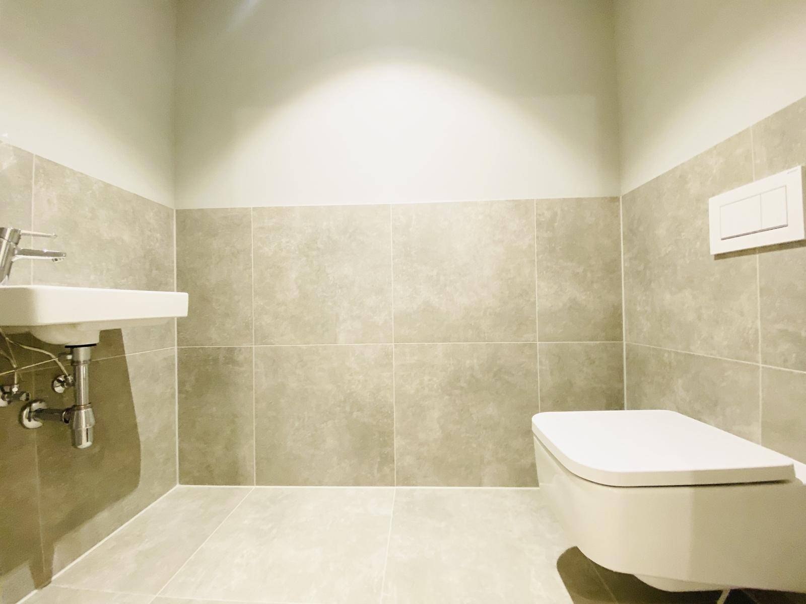 Modernes Gäste-WC mit Wand-WC, kleinem Waschbecken und hellgrauen Fliesen.
