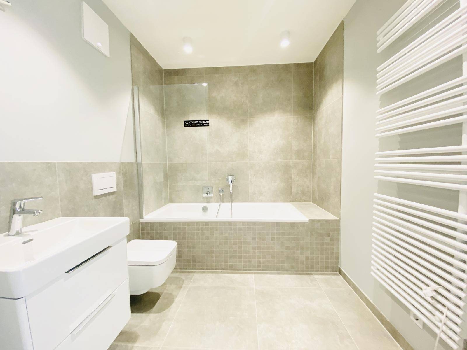 Modernes Badezimmer mit Badewanne, Dusche und beheiztem Handtuchhalter in hellen Grautönen.