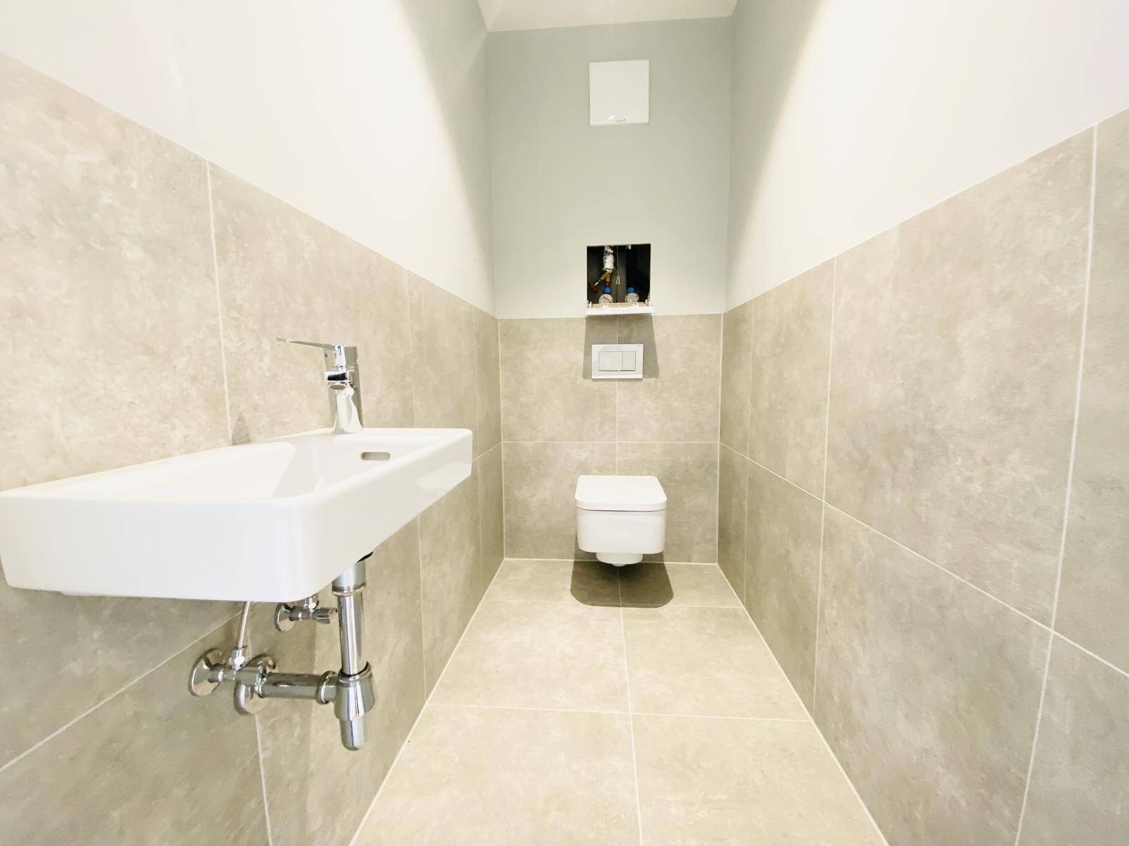 Modernes Gäste-WC mit Wand-WC, kleinem Waschbecken und grauen Fliesen.