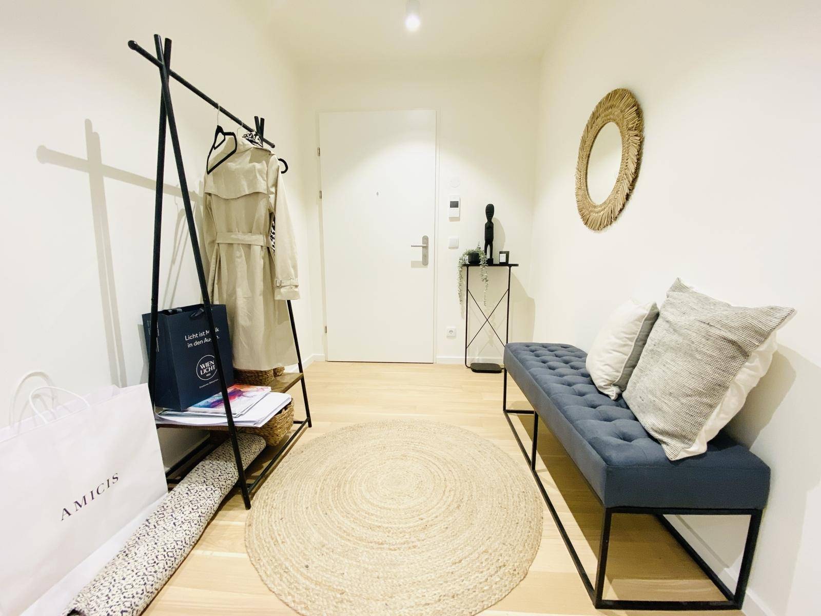 Heller Eingangsbereich mit Garderobe, Sitzbank und rundem Teppich auf Holzboden.