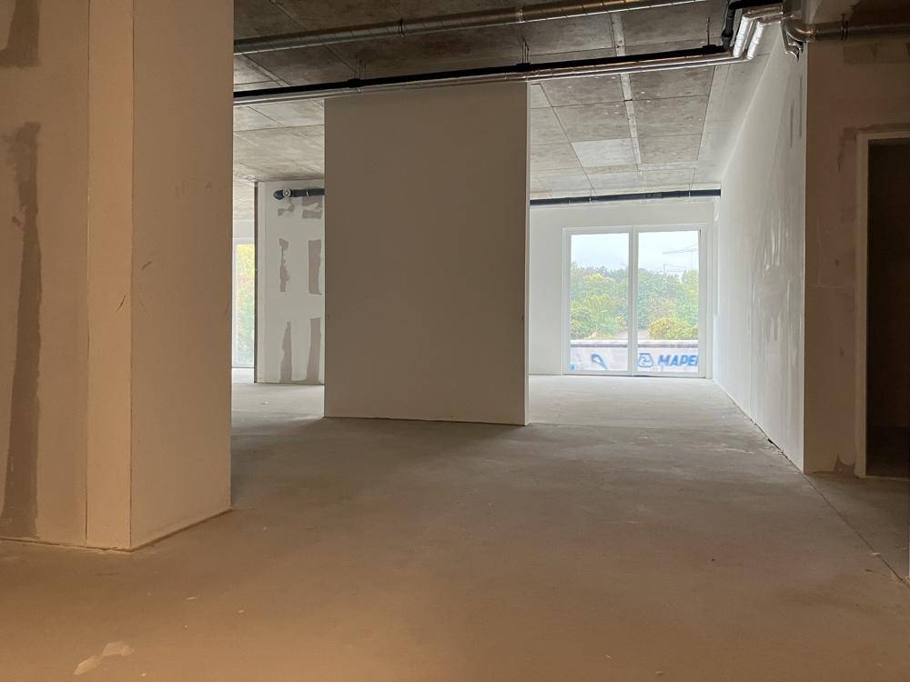 Offener Rohbau mit Säulen und großen Fenstern, die einen Blick ins Grüne ermöglichen.