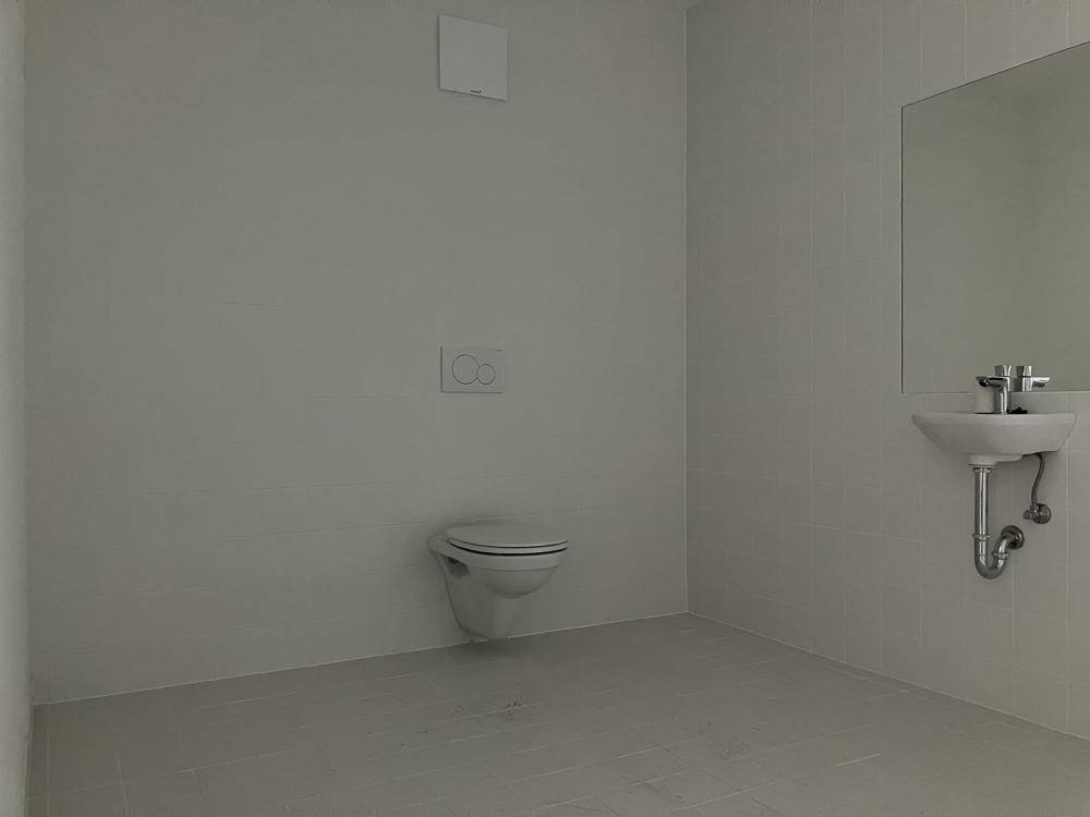 Modernes, hell gefliestes WC mit wandhängender Toilette und kleinem Waschbecken.