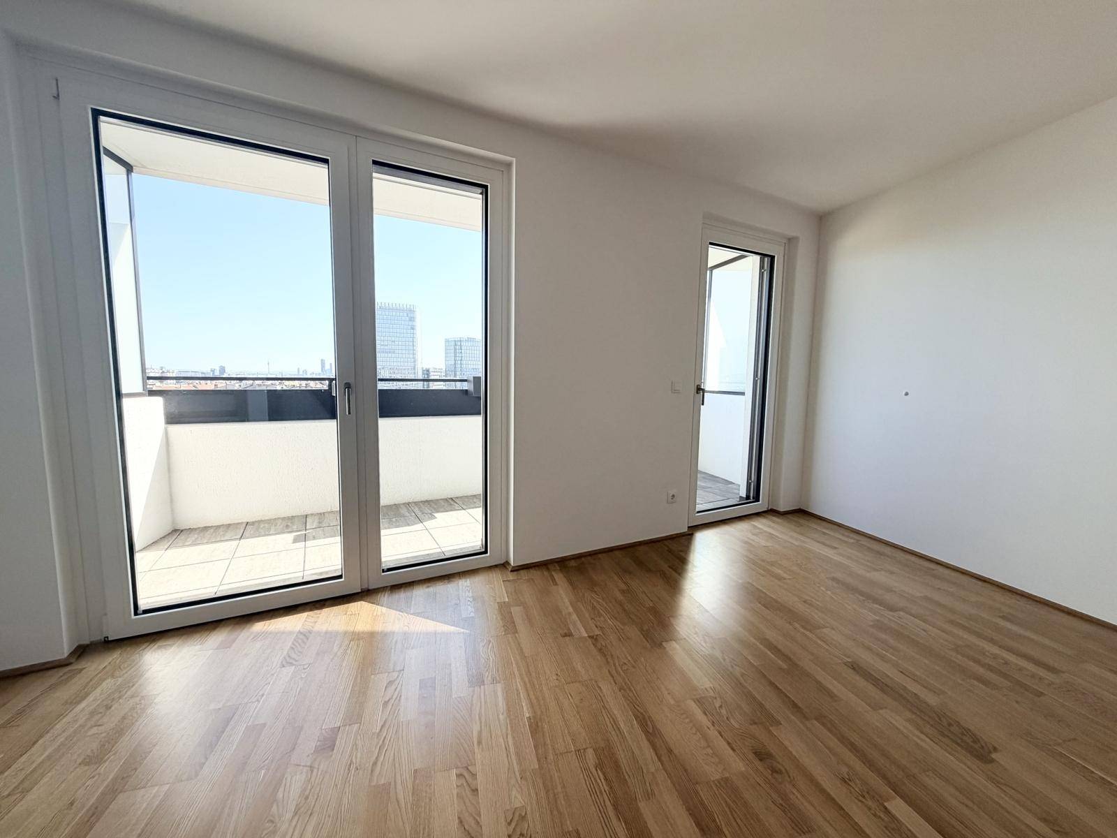 Helles Zimmer mit Holzboden und Zugang zu einem Balkon mit Stadtblick.