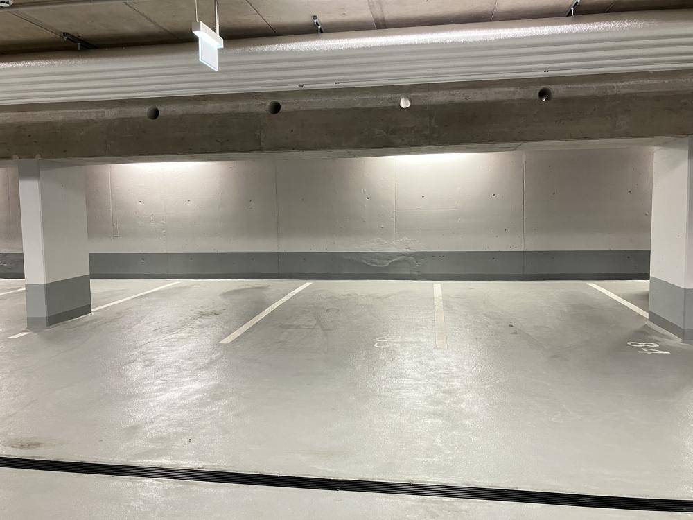 Leere Parkplätze in der Tiefgarage mit klaren Markierungen und Betonwänden.