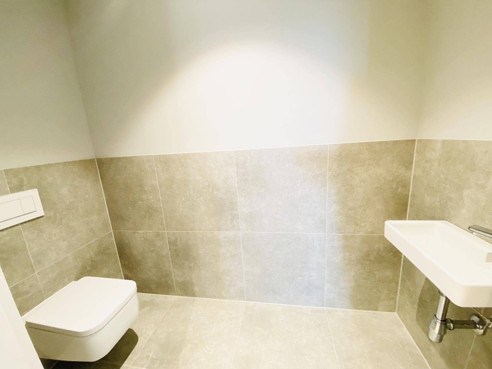 Kleines Gäste-WC mit Wand-WC und Waschbecken, halbhoch gefliest in neutralen Tönen.
