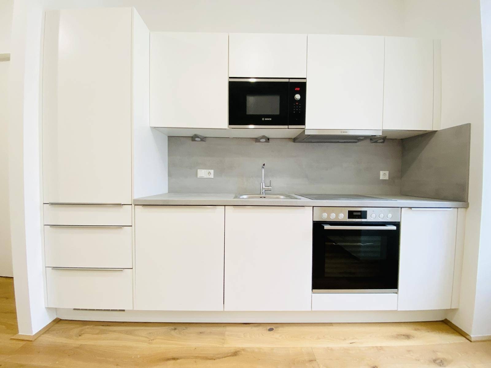 Moderne Einbauküche mit weißen Fronten, integriertem Backofen und Mikrowelle.
