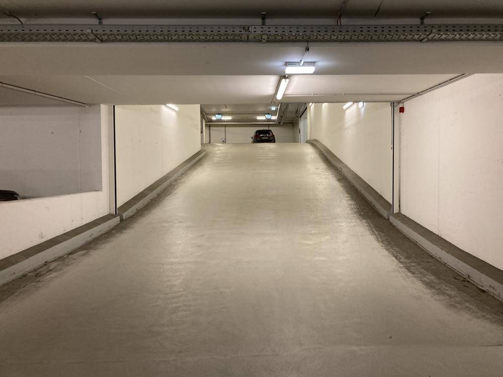 Auffahrtsrampe in einer modernen Tiefgarage mit heller Beleuchtung und klaren Linien.