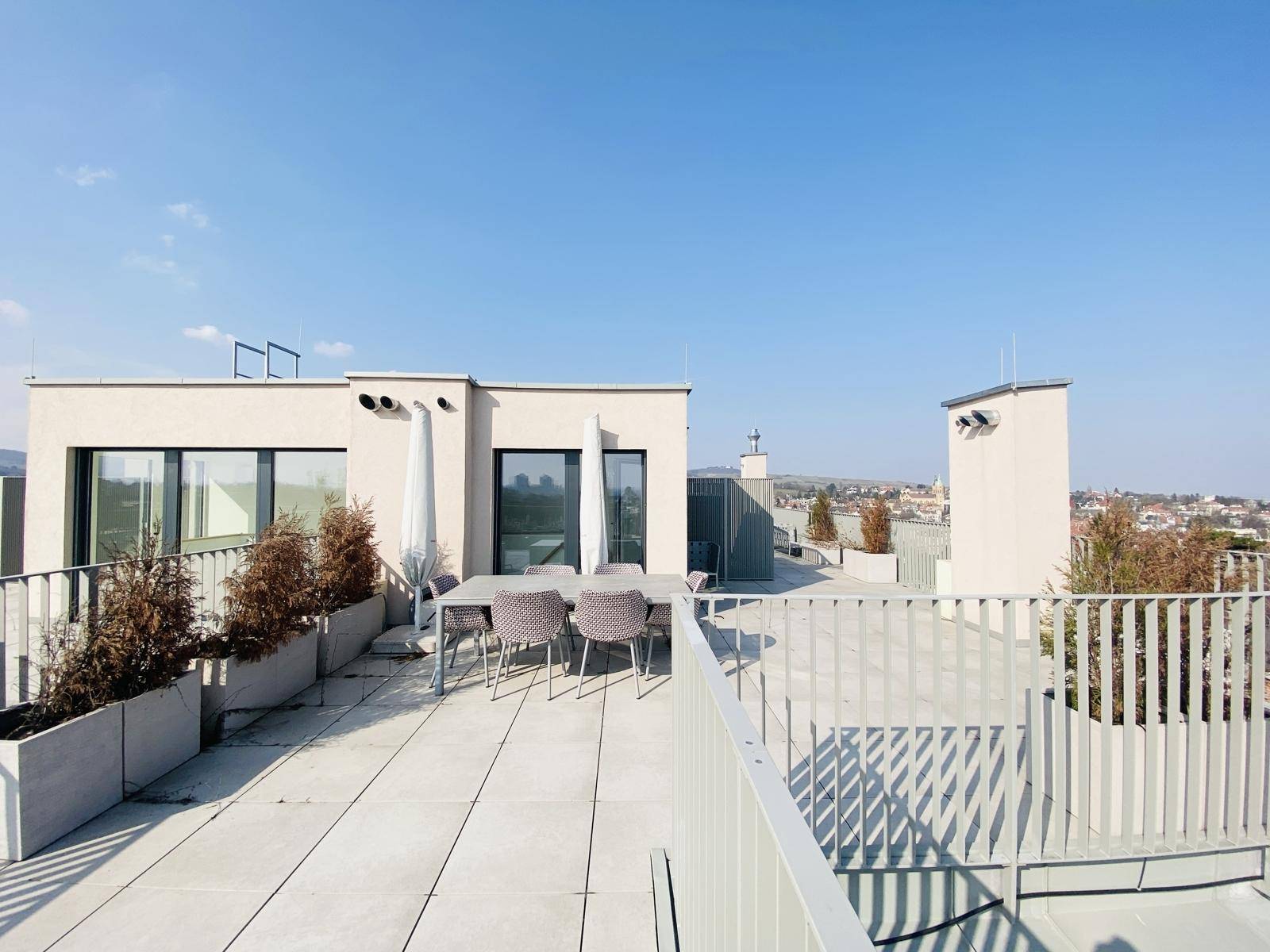 Sonnige Dachterrasse mit Sitzgelegenheiten und Blick auf die umliegenden Dächer und Hügel.