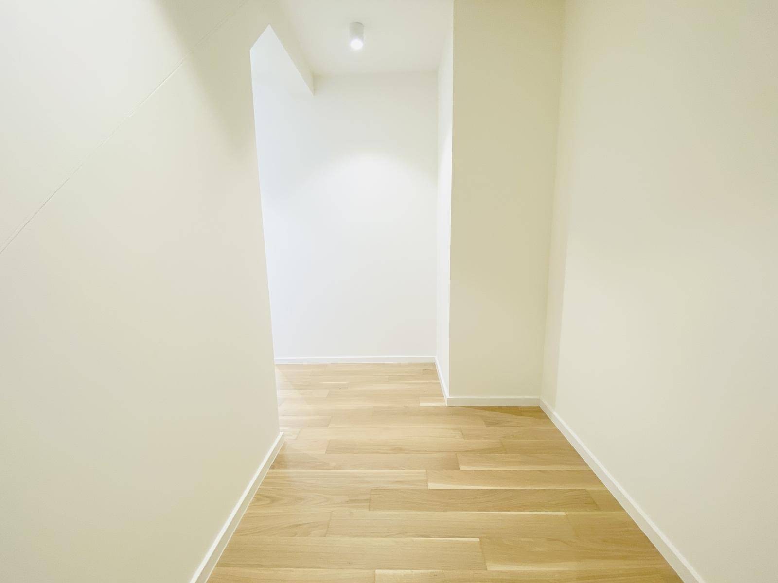 Moderner Flur mit hellem Holzboden und schlichten, weißen Wänden.