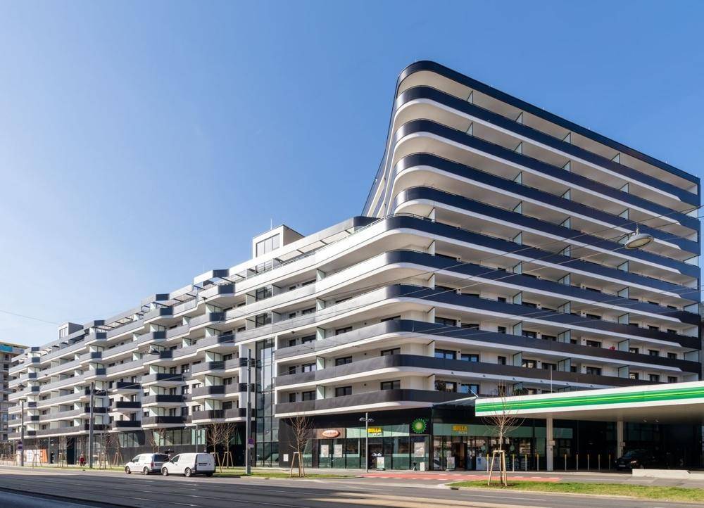 Moderne Wohngebäude-Fassade mit geschwungenen Balkonen und großen Fenstern in urbaner Umgebung.
