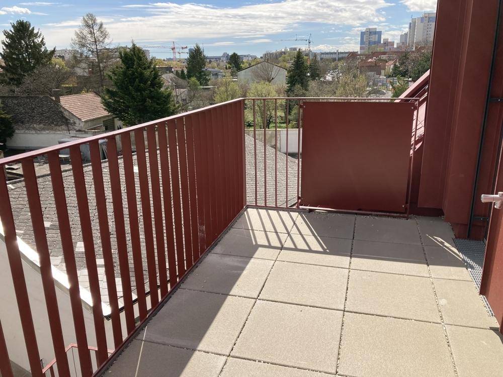 Geräumiger Balkon mit rotem Geländer und Fliesenboden, bietet einen weiten Stadtblick.