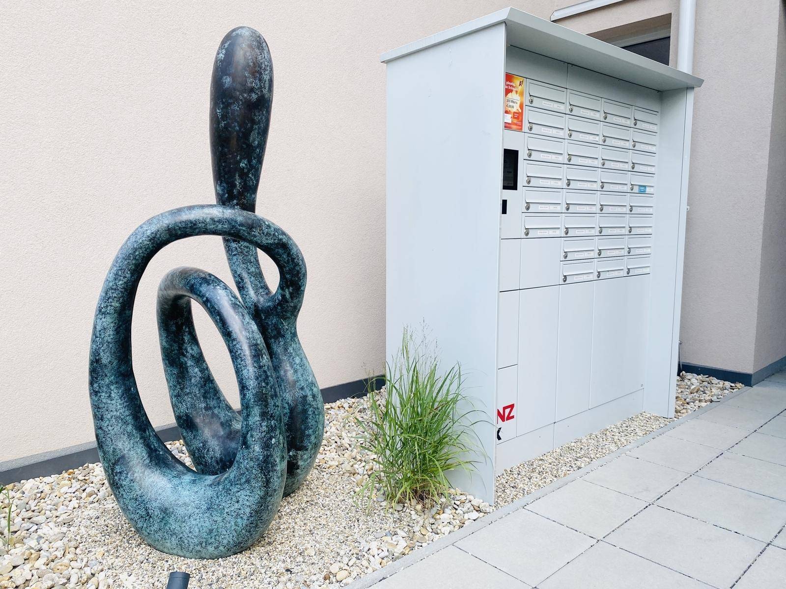 Moderner Eingangsbereich mit Briefkästen und einer abstrakten Skulptur im Außenbereich.