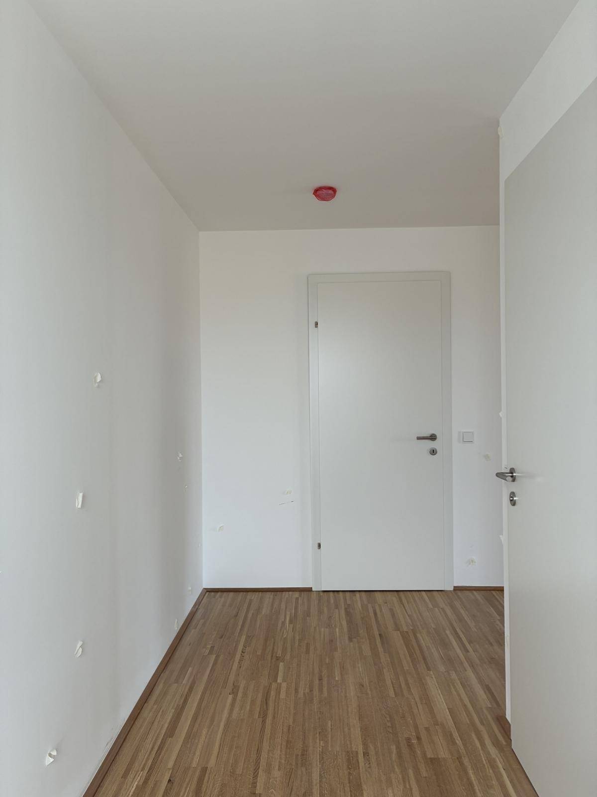 Heller Flur mit Holzboden und weißen Wänden, der zu weiteren Räumen im Neubau führt.